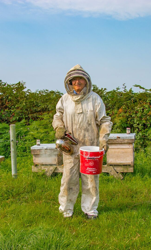 Farmer in beekeepers gear in front of hives