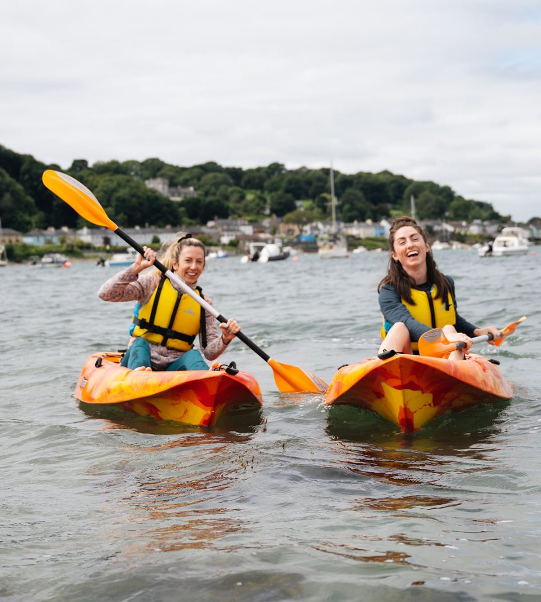 Two women rowing kayaks in a bay